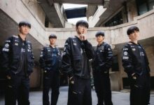 Five young men in matching black jackets stand together.