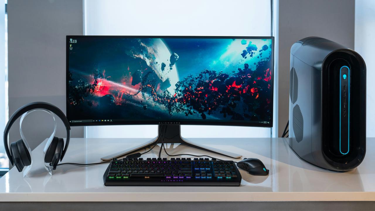 A curved computer monitor, tower, keyboard, mouse, and headphones on a white desk